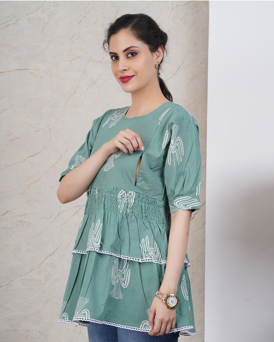 Woman wearing a nursing friendly green patterned dress with two feeding zips against a neutral background.