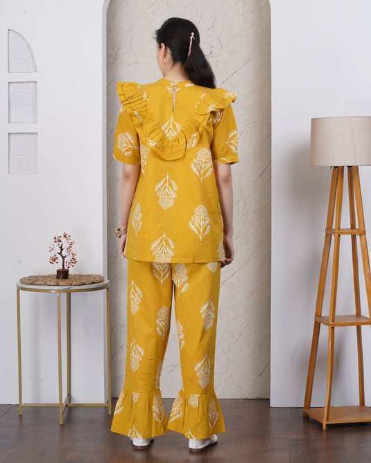 Woman wearing a yellow outfit with white patterns in a minimal indoor setting.