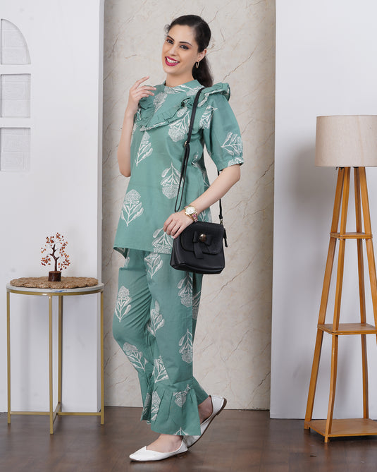 Woman in a green floral outfit holding a black handbag indoors.