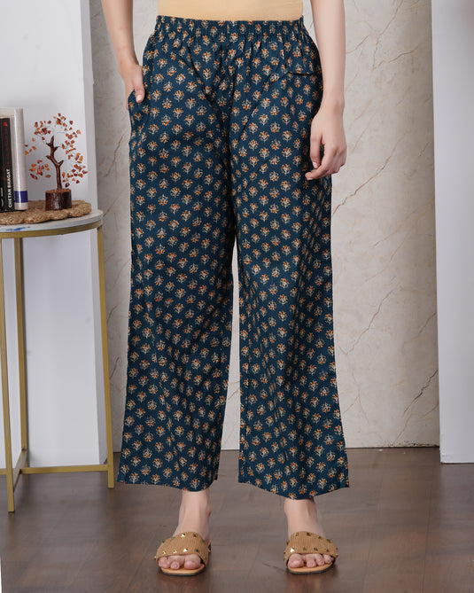 A person wearing dark teal wide-leg cropped pants with a beige and brown floral pattern, styled with tan slide sandals in an indoor setting.