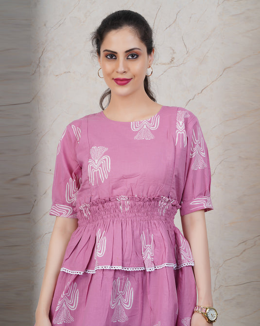 Woman wearing a pink dress with white patterns against a beige wall.