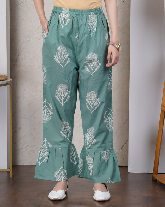 Woman wearing teal pants with white floral patterns against a neutral background