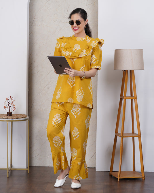 Woman in a yellow outfit holding a tablet in a room with a lamp and small table.