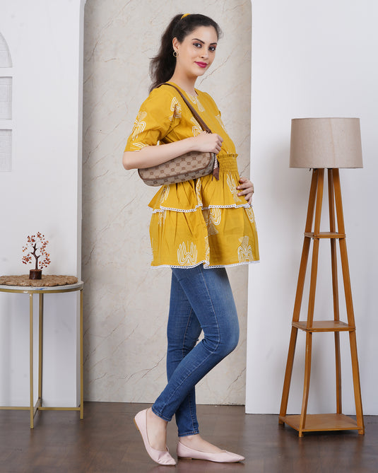 Pregnant Woman in yellow maternity top and blue jeans holding a brown bag indoors.
