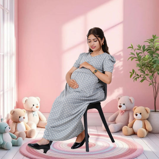 Pregnant woman in a gray dress sitting on a chair in a room with pink walls and teddy bears.
