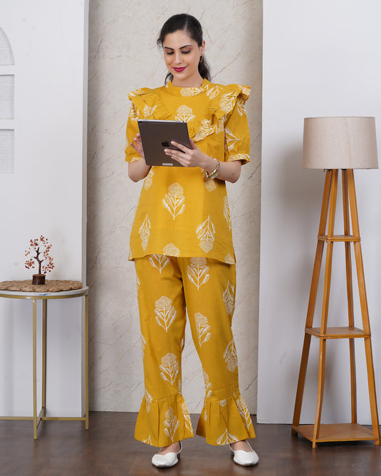 Woman in a yellow outfit with floral patterns standing indoors, holding a tablet.