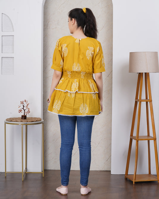 Woman wearing a yellow top and blue pants standing in a room with a lamp and small table.