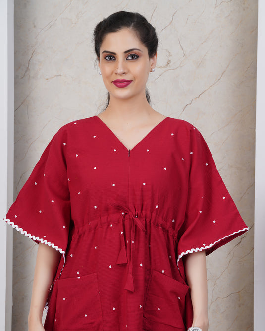 Woman wearing a red dress with white patterns against a beige wall.